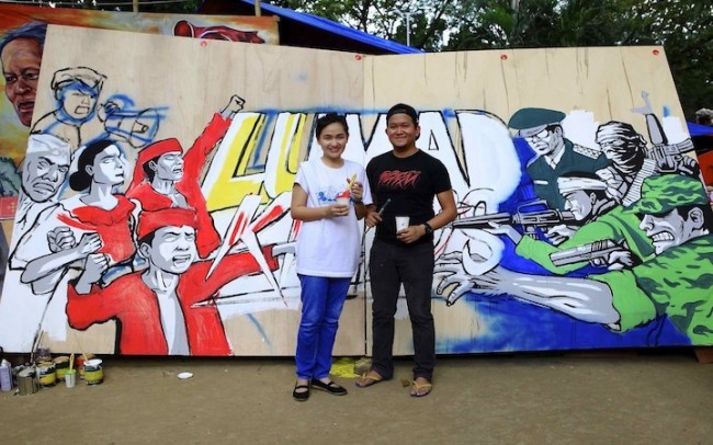 Gerilya artists Janno Gonzales and Mar Rios with their work in progress. The mural aims to bring awareness to the Lumad crisis in Mindanao. Photo by  Bernard Testa, InterAksyon.com.