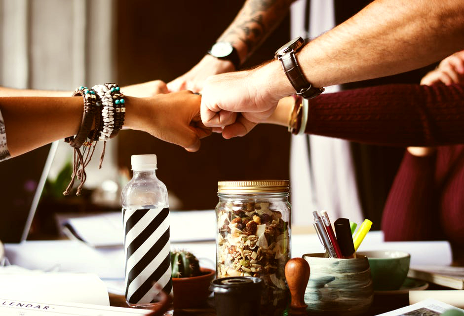 Five people's fists joined together over a table of school materials