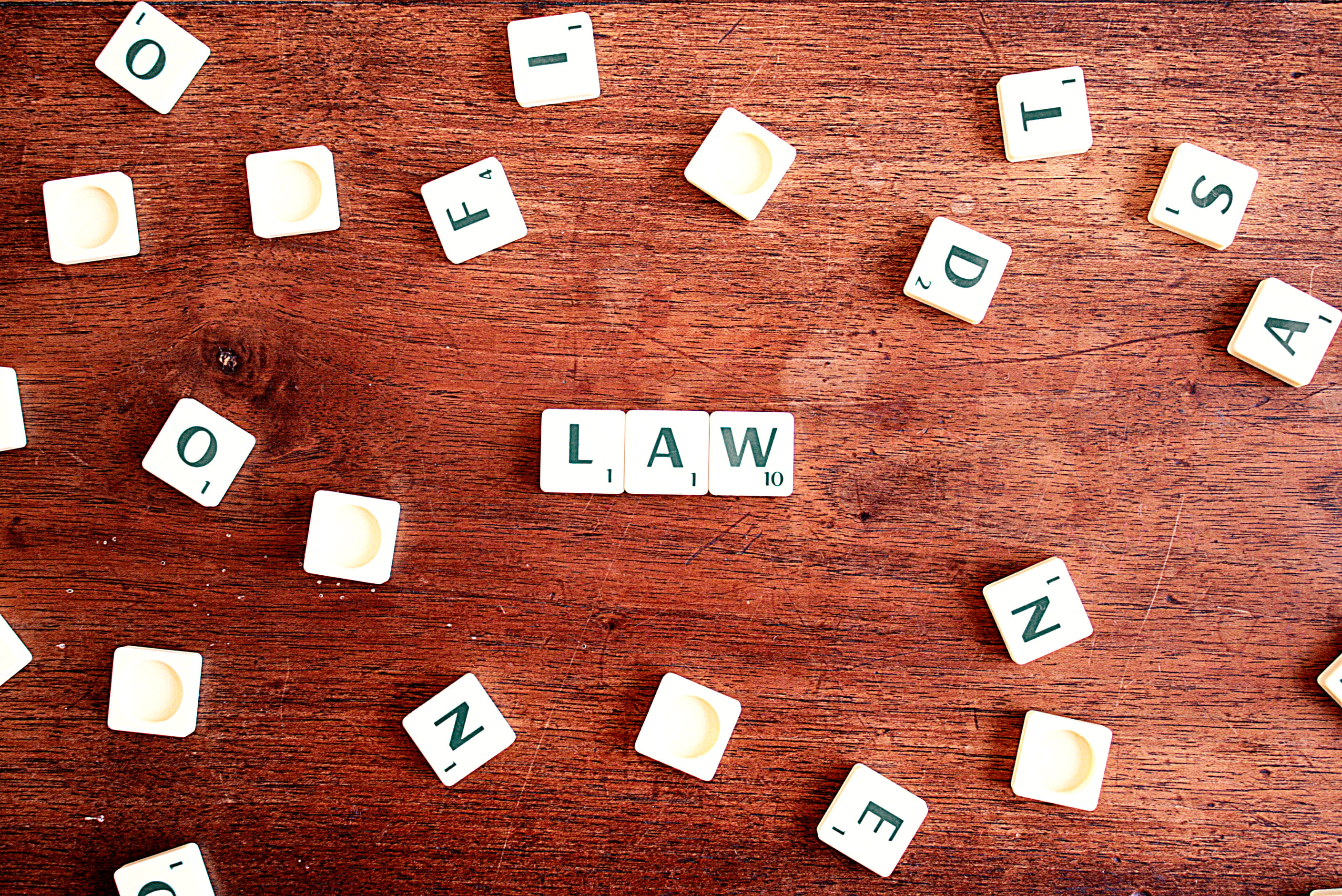 scrabble pieces scatter on a wooden table, with the word "law" spelled out in the middle