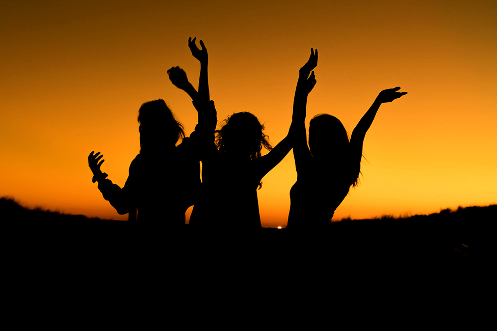 Silohoutte of three people waving their hands in sunset background
