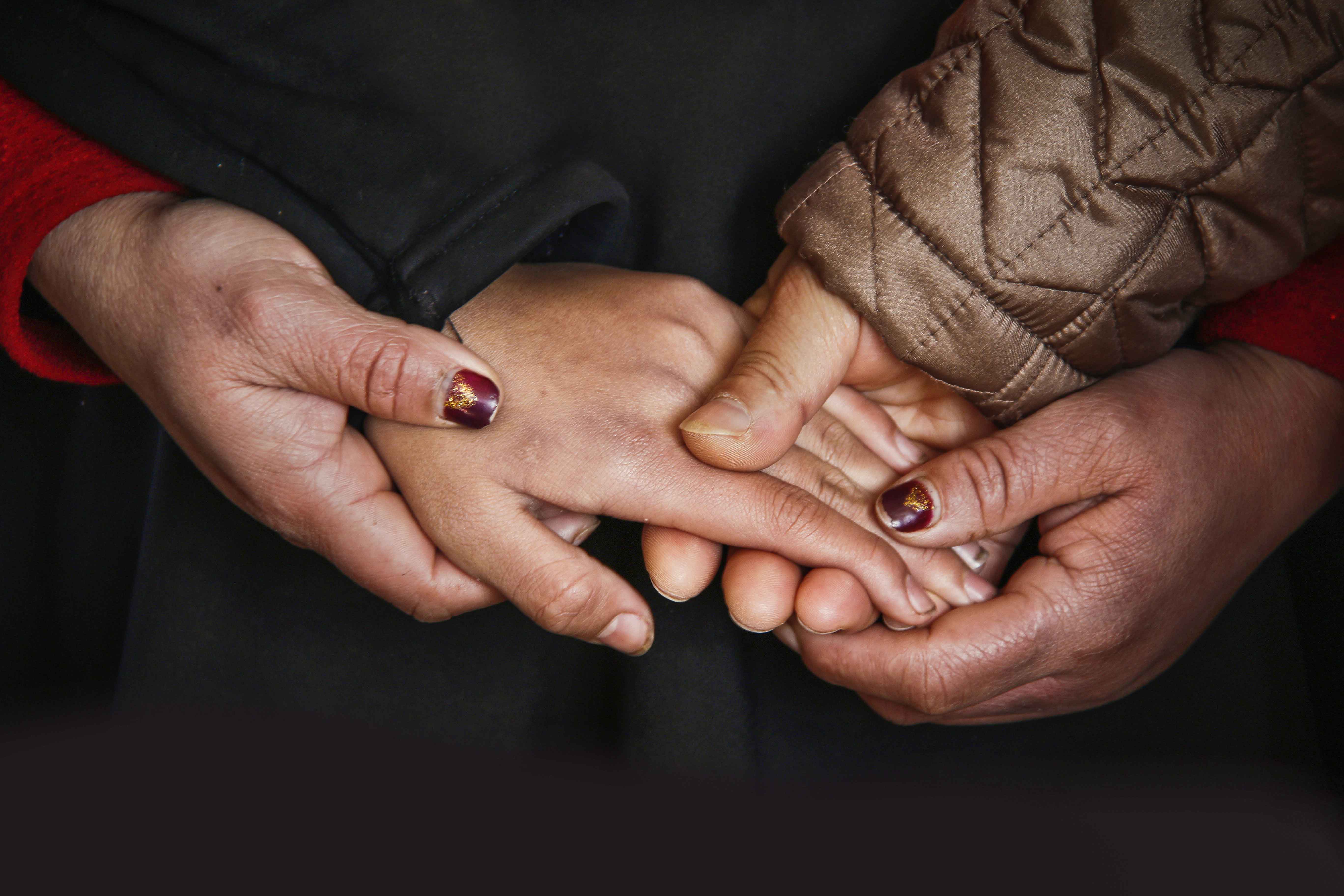 three adult's hands holding a young person's hand