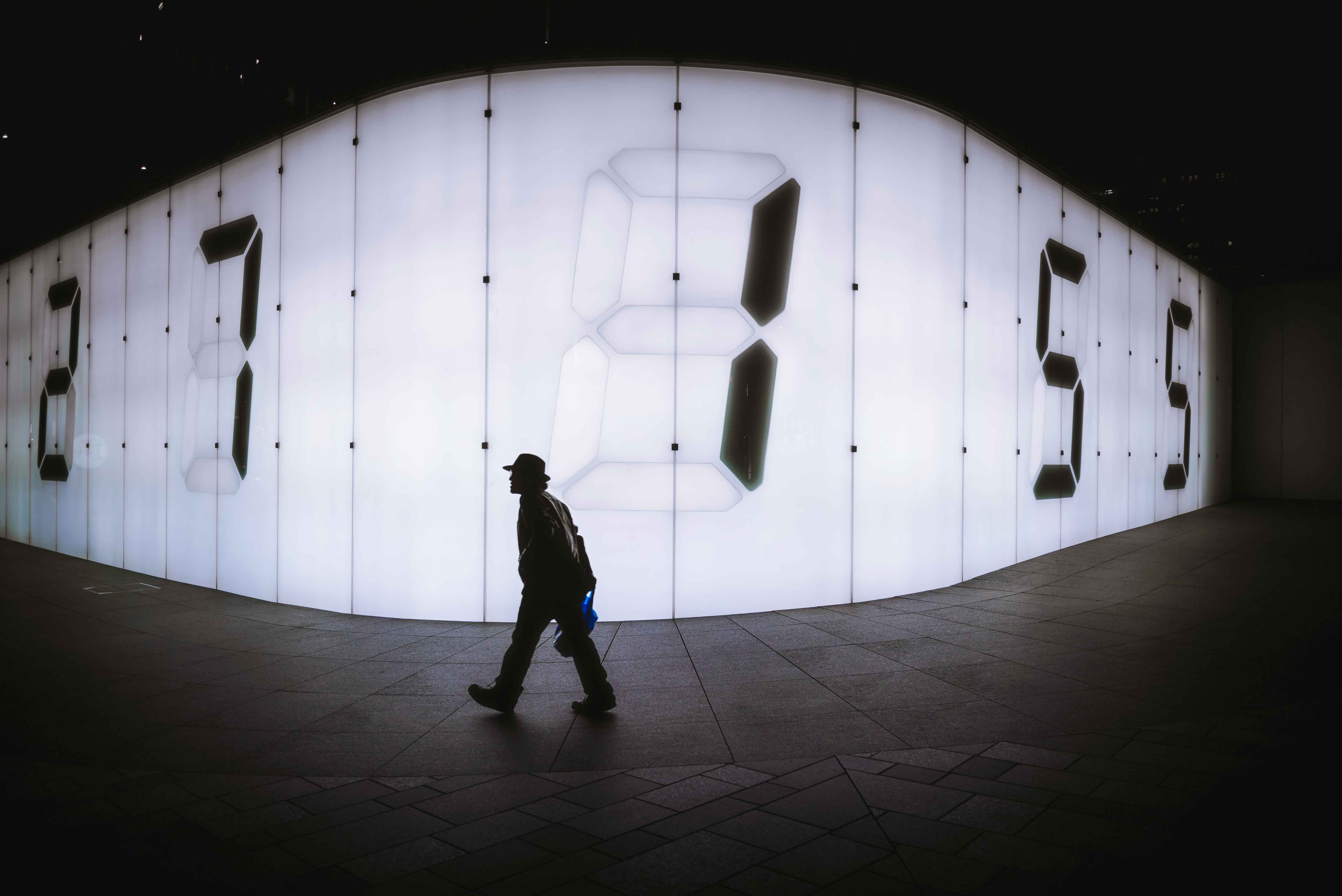 silhouette of man walking in front of an illuminated wall with huge numbers