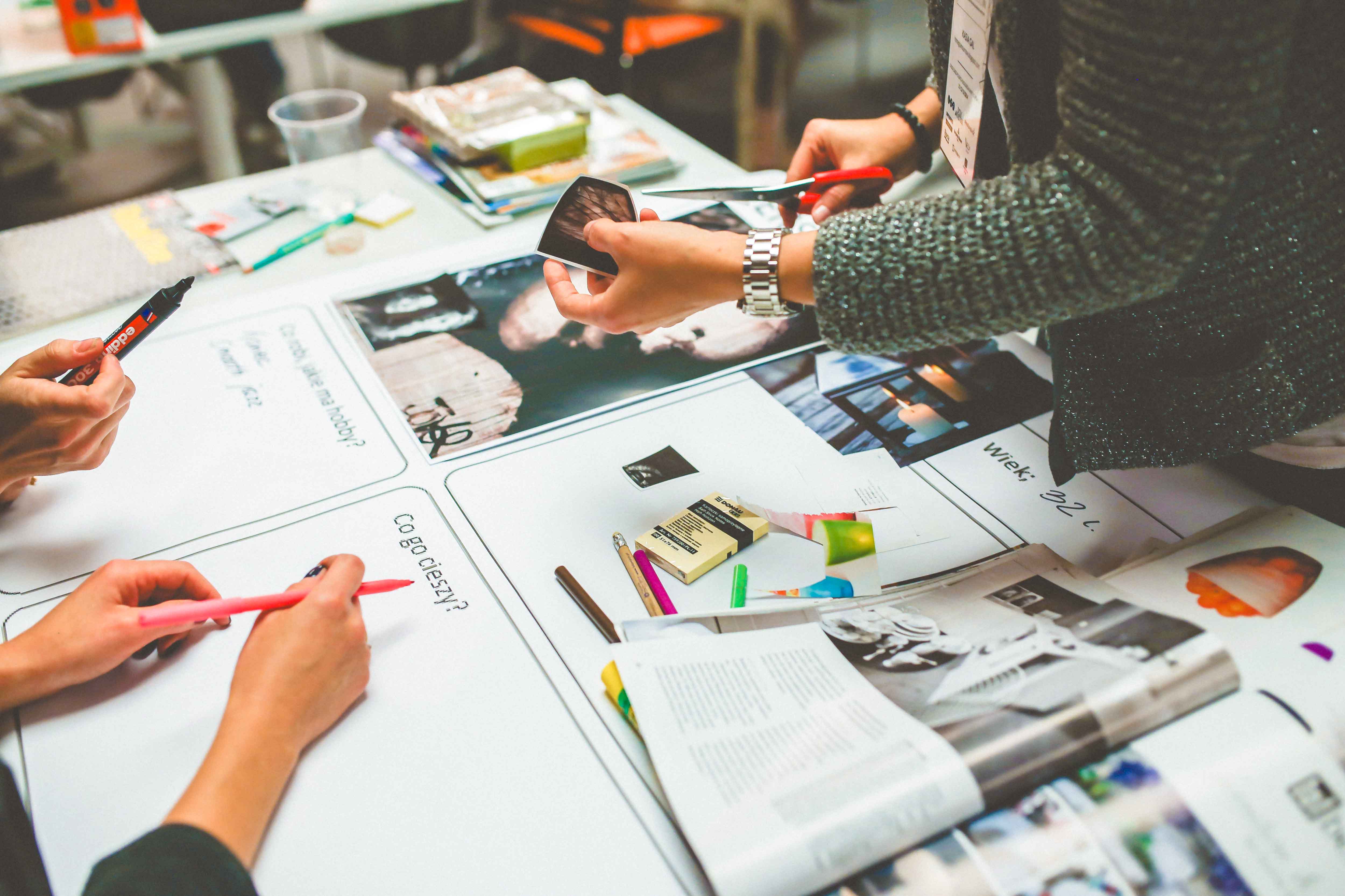women's hands, cutting out pictures and holding a pen. art materials and magazines spread across the table