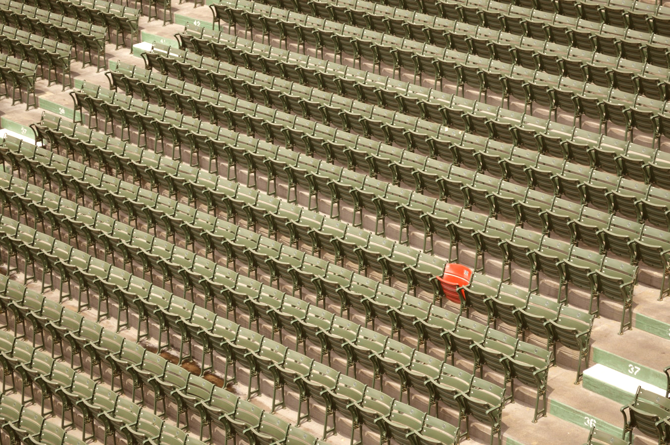 An auditorium with over a hundred gray chairs, with one red chair in the middle