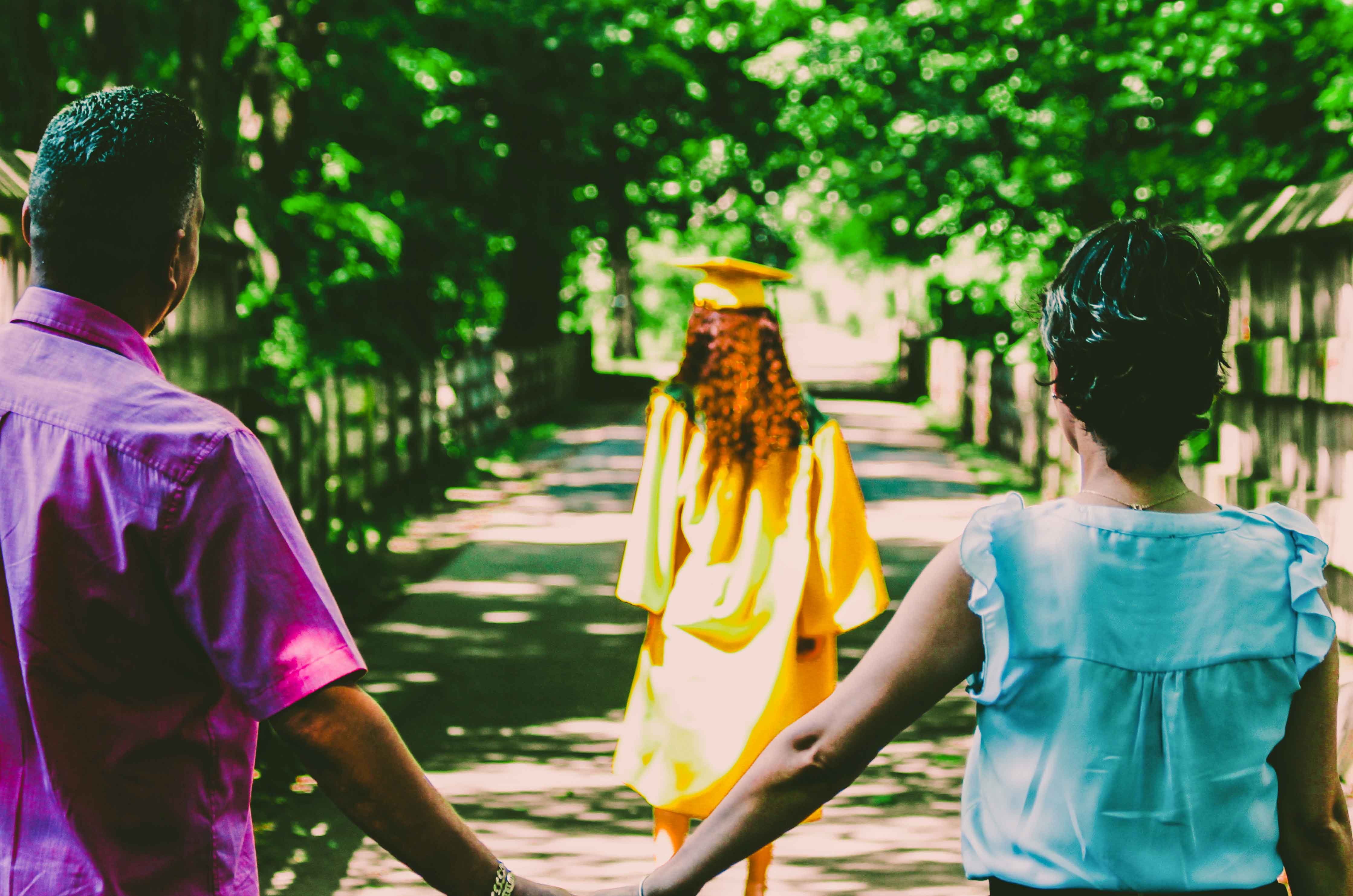 mother and father hold hands as they watch their daughter in a graduation toga walk away