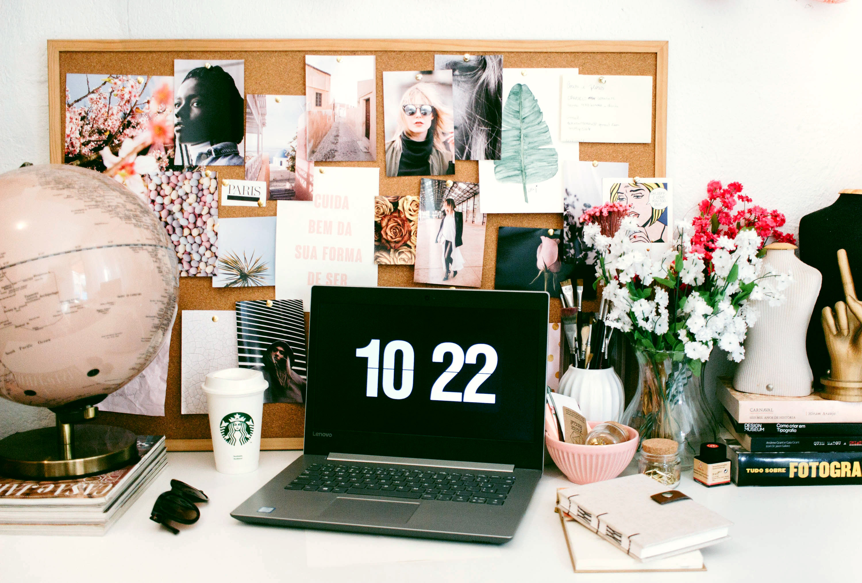 Laptop on a busy desk. Cork board filled with nice photographs on the wall