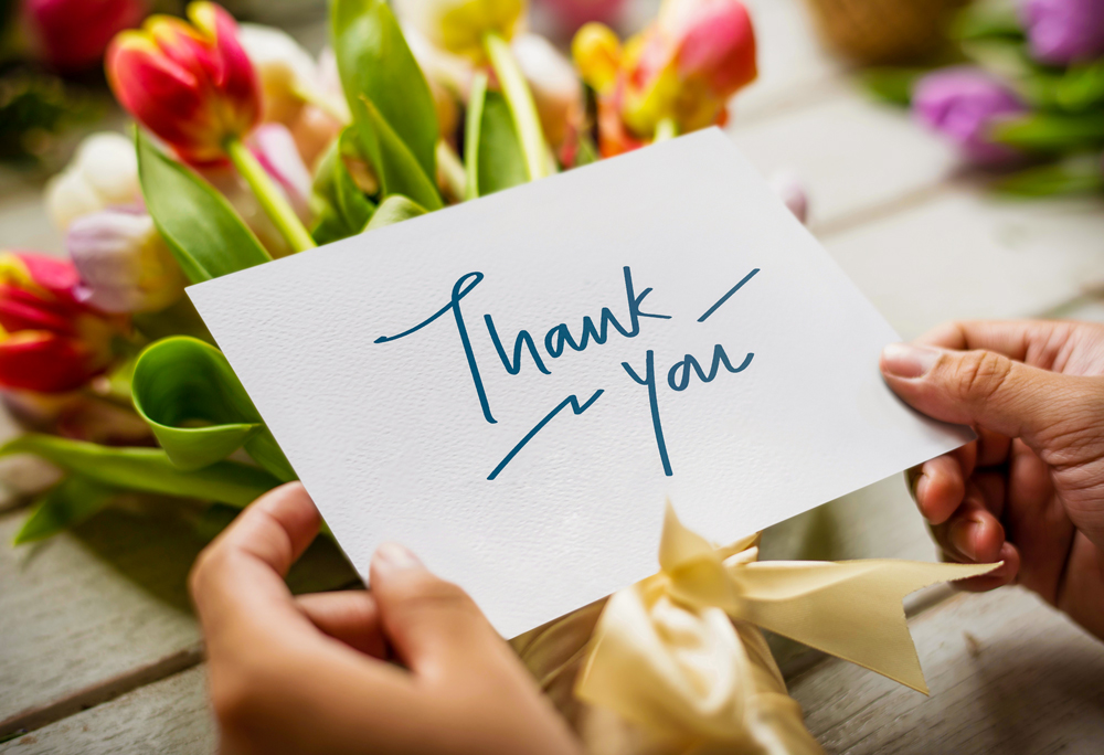 hands holding a "thank you" card over a bouquet of flowers