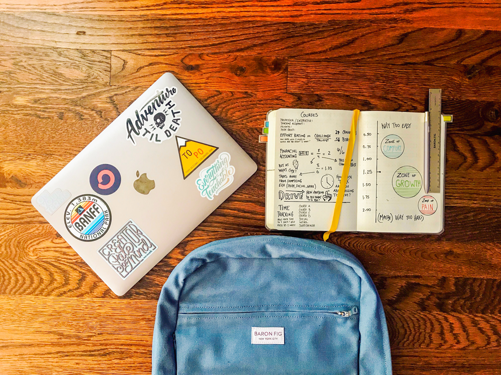 laptop with stickers, open notebook with notes, and a backpack on the floor