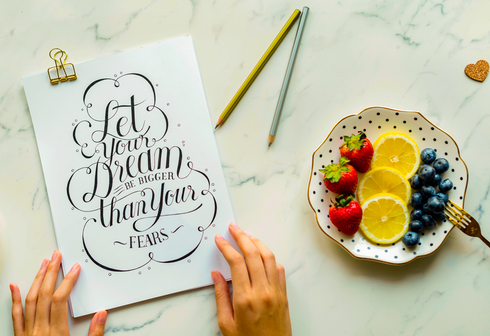 card laying on a table with the print 'Let your dreams be more than your fears' beside a plate with fruits