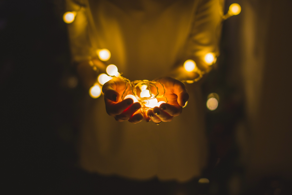 two hands holding out a string of glowing christmas lights