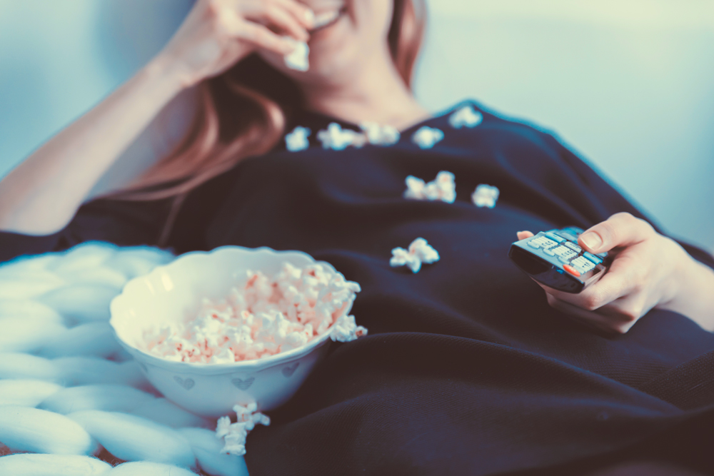 girl eating popcorn and holding a remote control