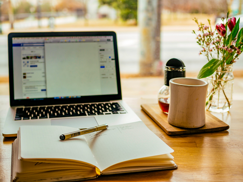 open laptop, notebook and pen, and mug on desk