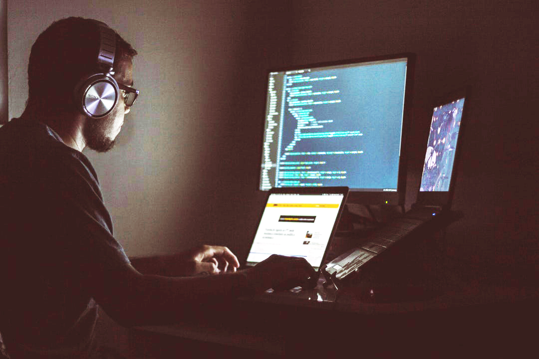 man programming on a laptop, simultaneously working on three screens
