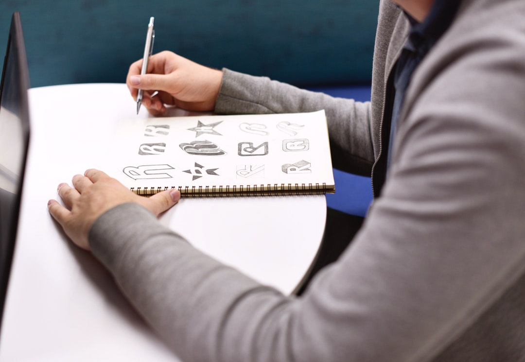 Someone's arm is shown drawing sketches on a notebook