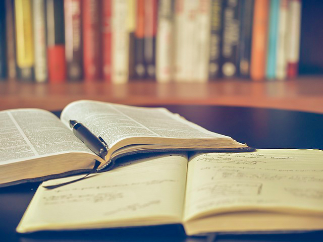 open book and notebook on a table in front of bookshelf