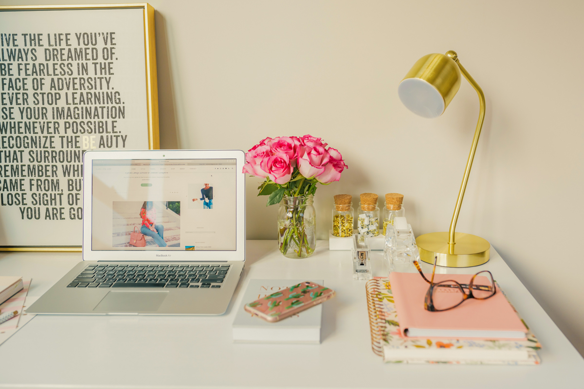 laptop, mobile phone, lamp, notebooks, glasses, and flowers on a desk