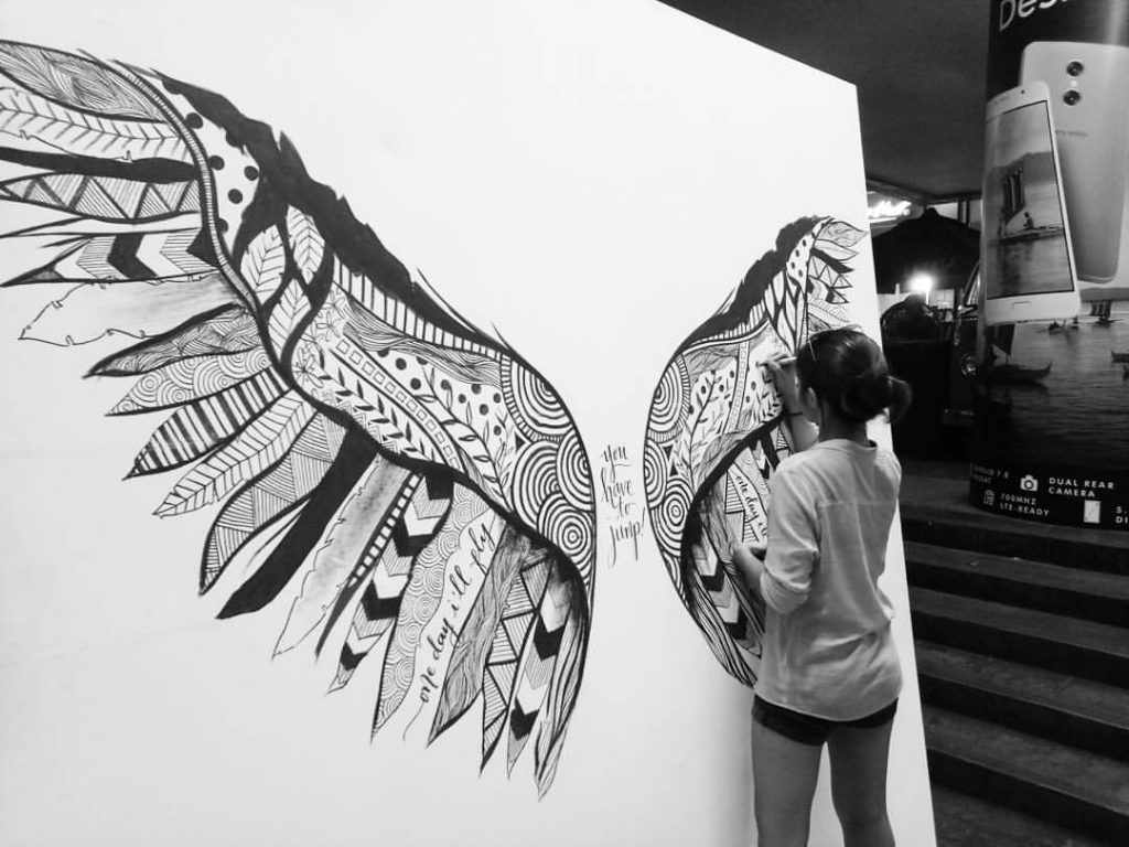 Details Ink founder Kara Pangilinan drawing a mural of wings