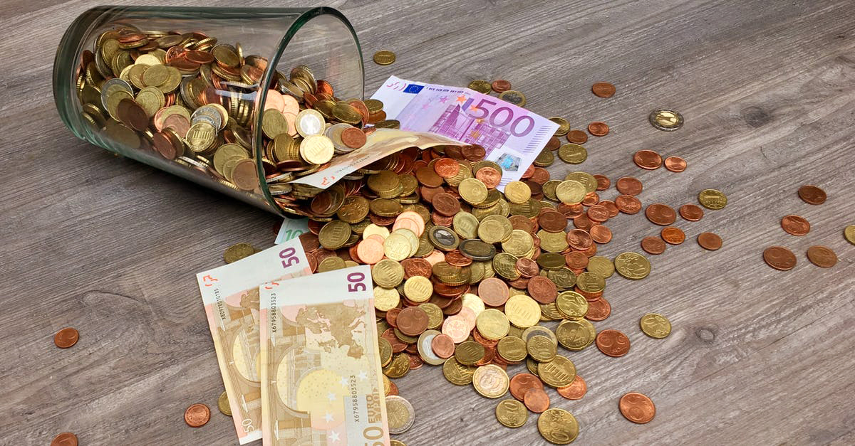 paper money bills and hundreds of coins spilling out of a glass