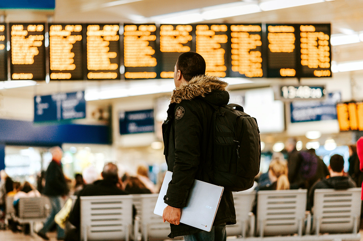 young man standing in front of flight schedule board in an airport
