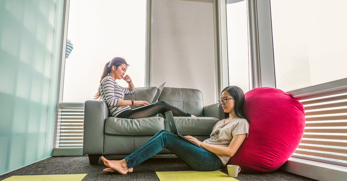 two girls sitting in a living room while using their laptops