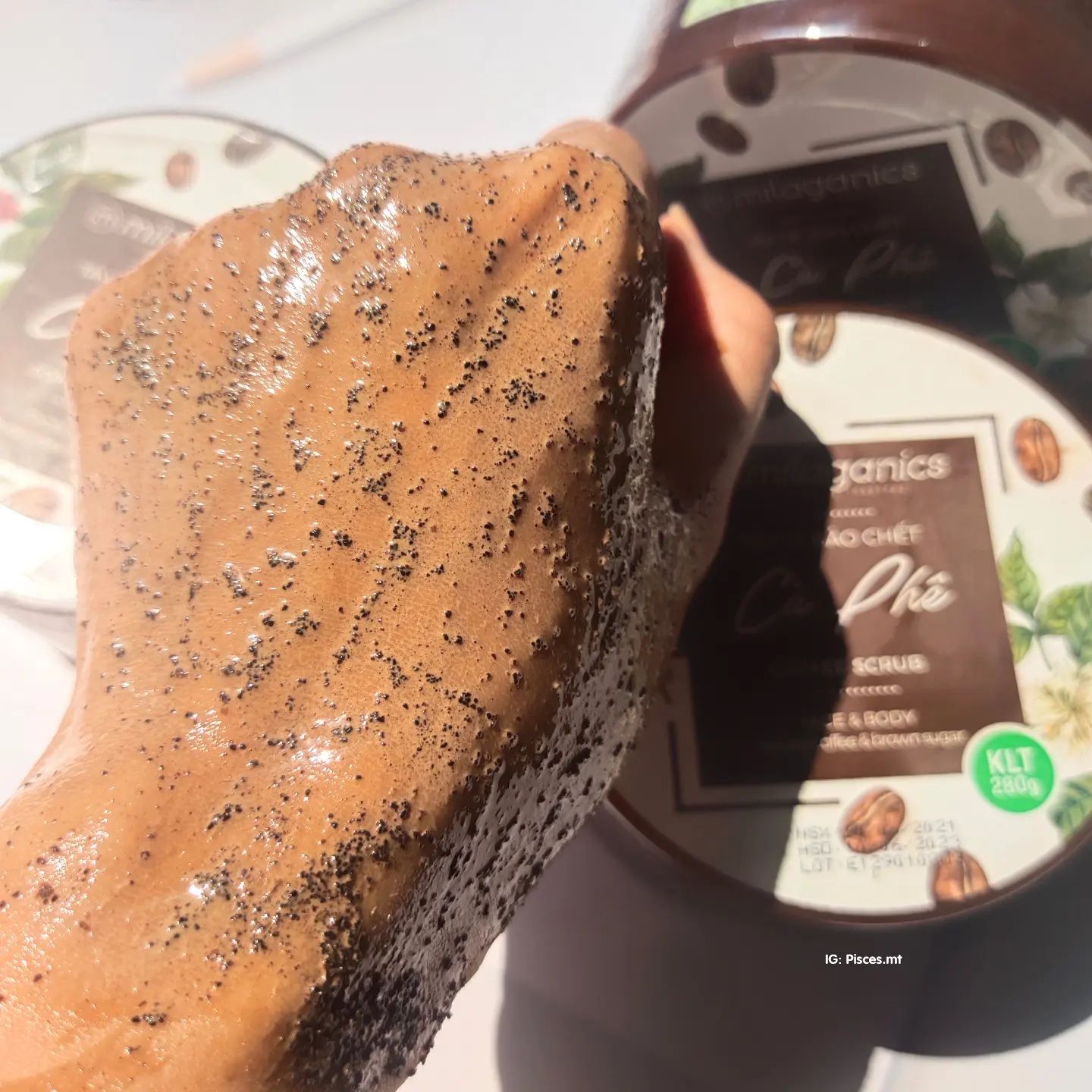 Sản phẩm tẩy da chết Milaganics đang được thử nghiệm, thể hiện trên bàn tay với lớp scrub cà phê, nhấn mạnh hiệu quả tẩy tế bào chết, giúp da mềm mại và dễ dàng thấm lotion. Review tẩy da chết Milaganics, ủng hộ mỹ phẩm local brand.