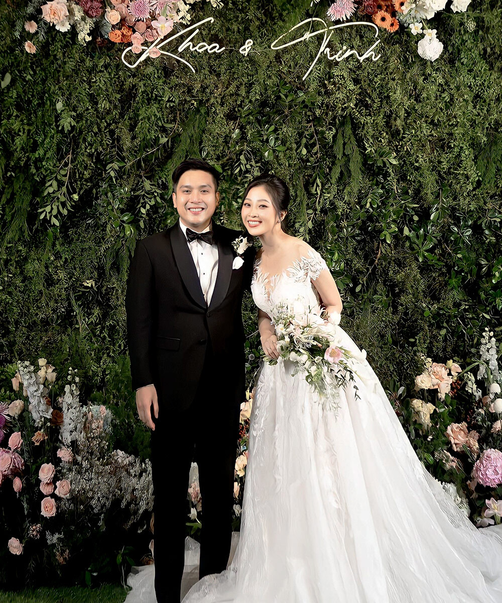 Cặp đôi hạnh phúc trong ngày cưới, cô dâu xinh đẹp trong trang phục đám cưới lộng lẫy với makeup cô dâu hoàn hảo. Cảnh nền hoa tươi tạo không khí rộn ràng, thể hiện sự ấm cúng và ý nghĩa của ngày 10.10 tại lễ cưới Anh Tú và Diệu Nhi.