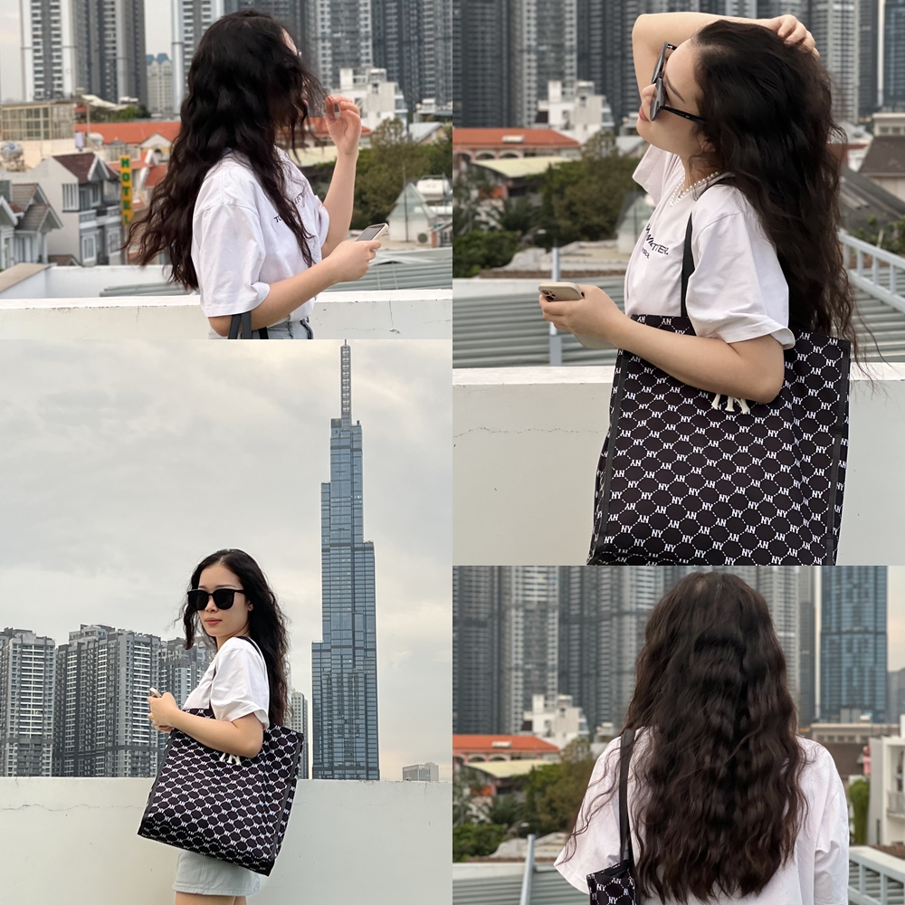 Cô gái sinh năm 1998 đang tạo dáng với mái tóc uốn sóng xinh đẹp, bên cạnh tòa nhà chọc trời. Hình ảnh thể hiện sự tự tin và phong cách của người yêu thích làm đẹp, mang theo túi xách thời trang, phản ánh sự nổi bật của thương hiệu Halio trong cộng đồng Gen Z.