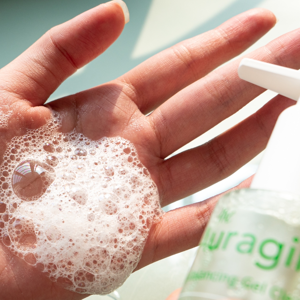 Bọt xà phòng từ gel rửa mặt The Auragins trên tay, thể hiện quá trình làm sạch da trong quy trình thải độc da sau Tết. Sản phẩm này giúp cải thiện tình trạng da mụn và xỉn màu nhờ vào các bước thải độc với bộ ba mỹ phẩm giá dưới 100K.