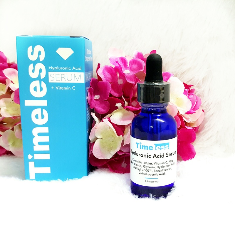 Sản phẩm serum axit hyaluronic Timeless với vitamin C cho da, nằm bên cạnh bao bì. Chứa các thành phần như nước, vitamin C, glycerin, axit hyaluronic giúp cấp ẩm và làm trẻ hóa da.