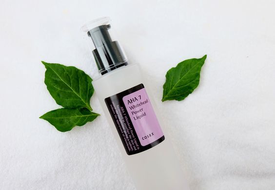 Chai tinh chất dưỡng da AHA 7 Whitened Power Liquid của COSRX, đặt trên nền vải trắng cùng với hai lá xanh, nhấn mạnh hiệu quả làm sáng da và chăm sóc da chuyên sâu.