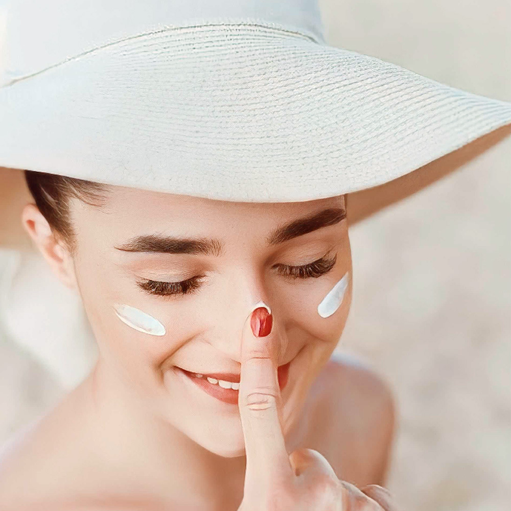 Người phụ nữ trẻ tuổi đang thoa kem lên mặt, gây sự chú ý với dấu ngón tay trên môi, thể hiện phong cách chăm sóc da mùa hè. Bài viết trên Lixibox khám phá thắc mắc có nên dùng retinol vào mùa hè không, cùng với các cách dùng retinol an toàn để không bị kích ứng hay đen sạm.