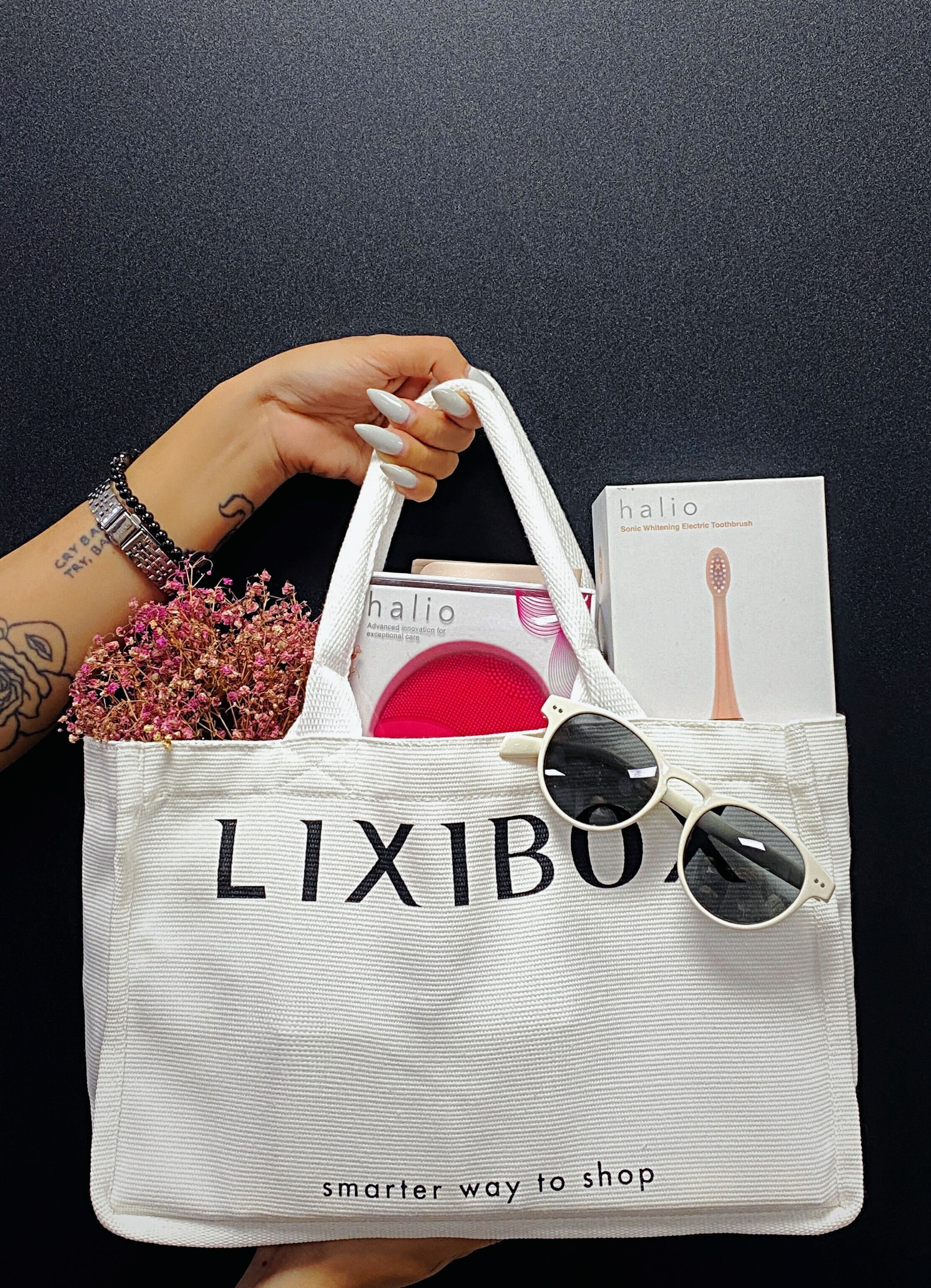 Bàn tay nữ với bộ quà GWP từ Lixibox gồm bàn chải điện và máy rửa mặt Halio cùng một chiếc túi Lixibox màu trắng, cho thấy cách thẩm mỹ và tiện ích trong việc chăm sóc sắc đẹp mà không tốn chi phí, liên quan đến chương trình GWP2010.