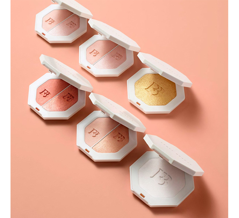 Bộ sản phẩm Fenty Beauty gồm các viên highlight và phấn má hồng với thiết kế tinh tế trên nền hồng. Fenty Beauty đã đổi mới các chuẩn mực trong ngành mỹ phẩm, từ trang điểm cho mẹ đến xu hướng son và kem nền.