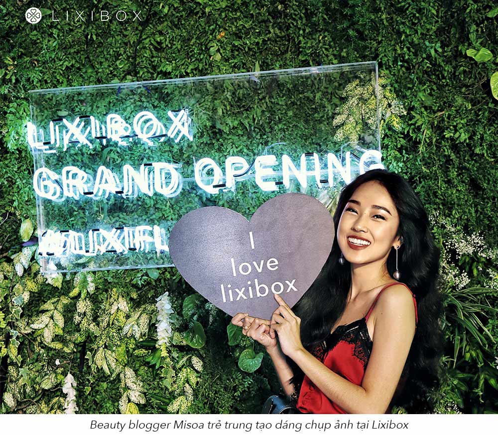 Sự kiện khai trương Lixibox Flagship Store thu hút đông đảo khách mời, trong đó có beauty blogger Misoa cầm biểu ngữ "I love Lixibox" bên cạnh biển hiệu rực rỡ "Lixibox Grand Opening".