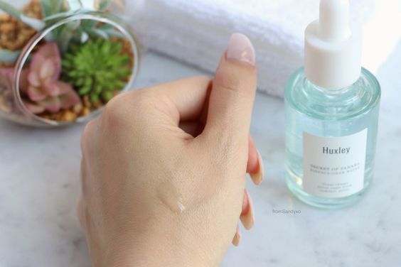 Hình ảnh bàn tay đang thoa tinh chất dưỡng ẩm Huxley trên nền đá trắng, cùng với một lọ sản phẩm dưỡng da Huxley. Bài viết hướng dẫn chu trình dưỡng da trong 30 ngày với bộ sản phẩm dưỡng ẩm cho da khô.