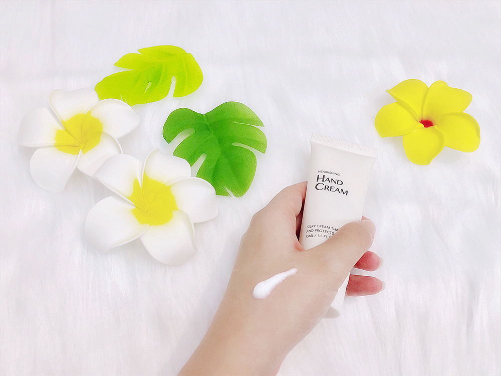Bàn tay đang cầm tuýp kem dưỡng tay trên nền hoa lá, nhấn mạnh tầm quan trọng của việc chăm sóc da tay để tránh những phút nắm tay ngượng ngùng khi gặp crush.