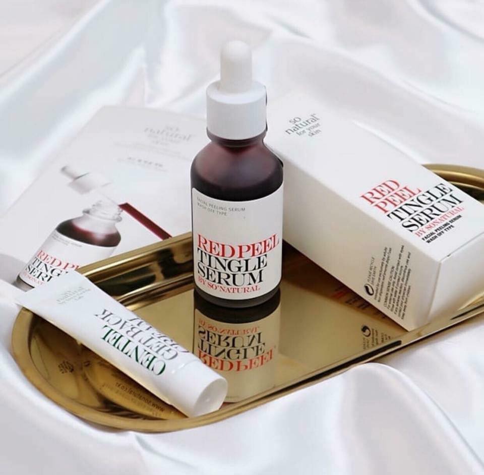 Hình ảnh sản phẩm serum tẩy tế bào chết Red Peel Tingle Serum từ So Natural, đang nằm trên khay vàng cùng với hộp sản phẩm, phù hợp cho quy trình chăm sóc da cơ bản, giúp cải thiện tình trạng da mụn hiệu quả.