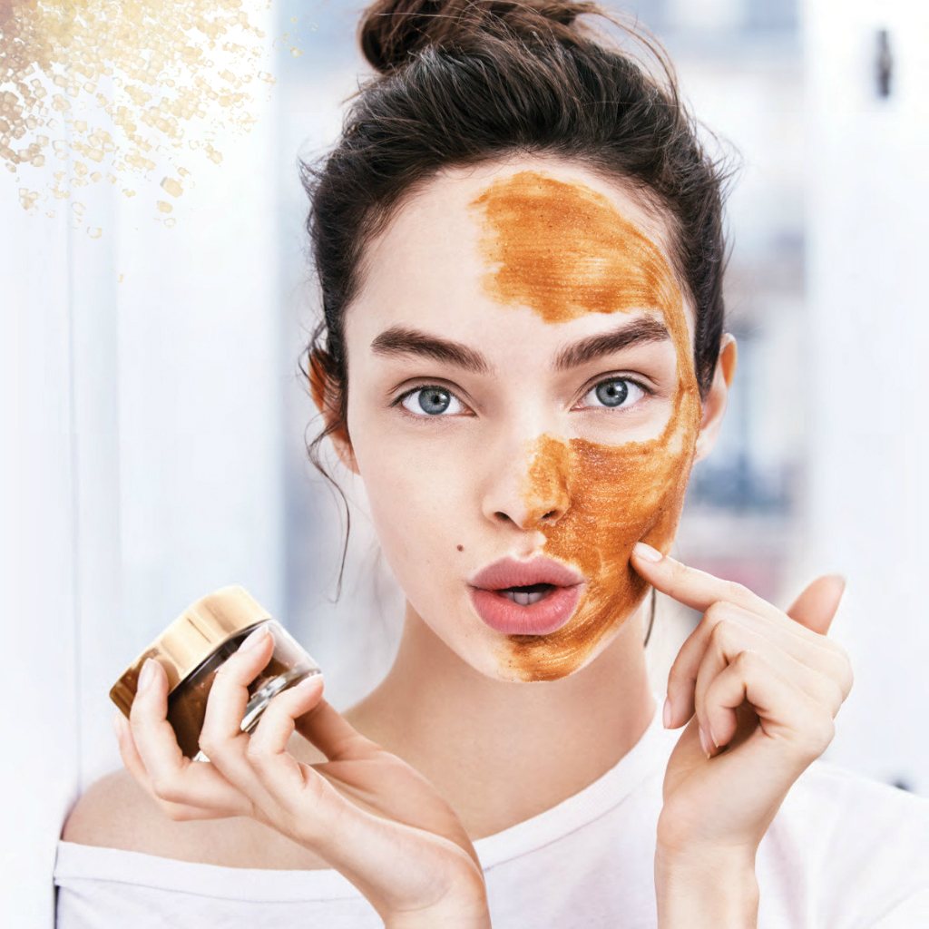 Một người phụ nữ trẻ chăm sóc da mặt với mặt nạ màu nâu, thể hiện quy trình dưỡng da cơ bản để có lớp nền trang điểm hoàn hảo và tránh tình trạng cakey, sần sùi.