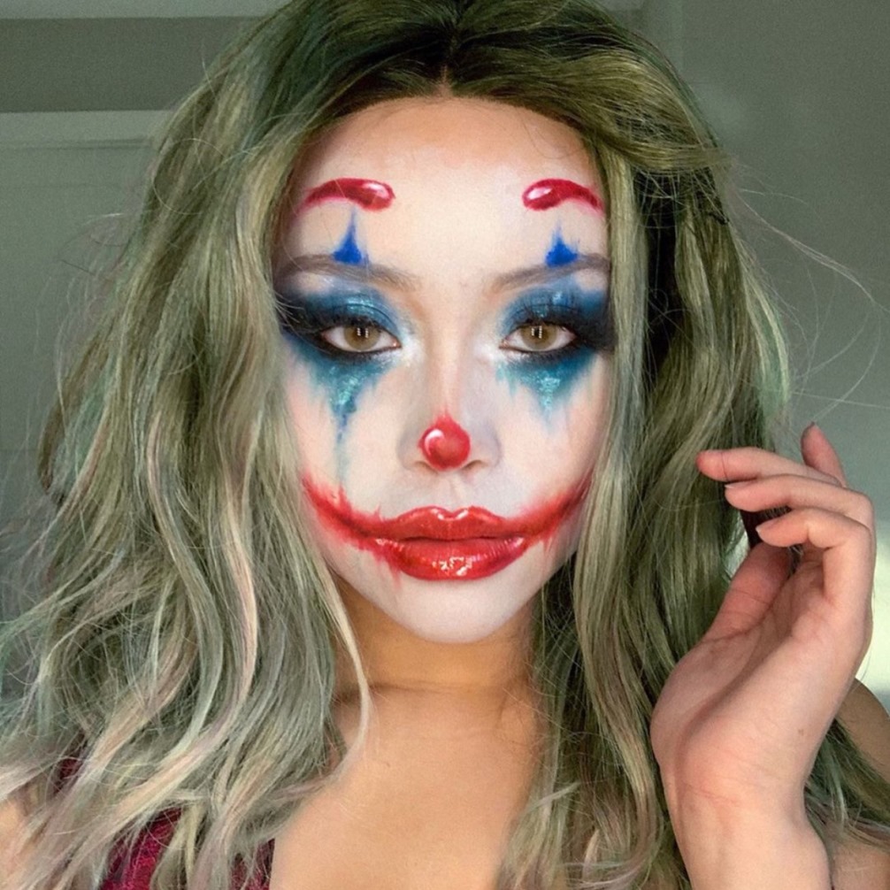 Hóa trang thành chú hề với lớp trang điểm cầu kỳ cho Halloween, kết hợp mái tóc dài xoăn màu xanh và lớp makeup nổi bật, mang lại phong cách ấn tượng cho buổi lễ hóa trang.