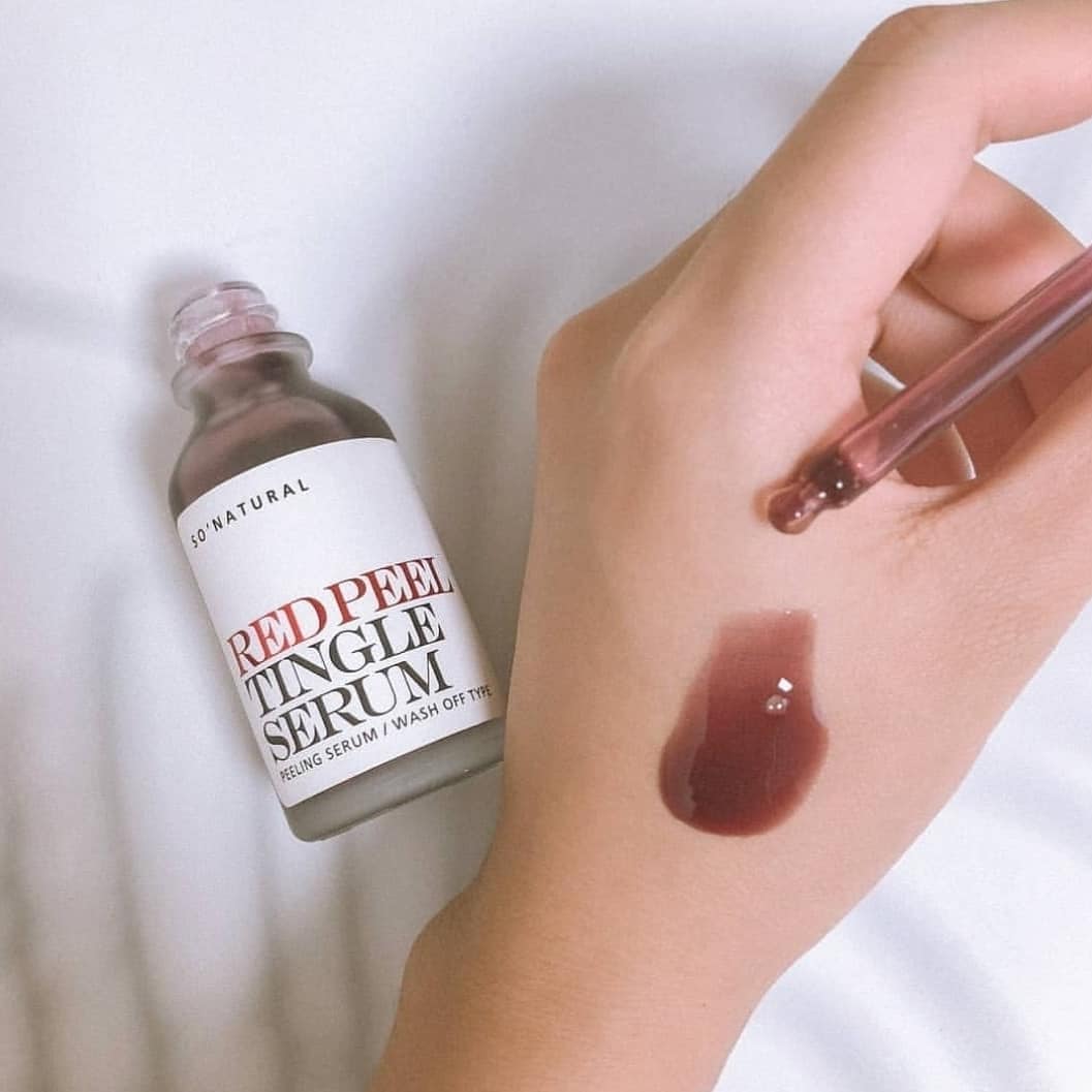 Chai serum Red Peel Tingle Serum So Natural đang được sử dụng trên tay, với một giọt serum màu đỏ đậm trên da. Sản phẩm nổi bật trong quy trình dưỡng da cơ bản, thu hút sự chú ý trong cộng đồng chăm sóc da nhờ hiệu quả nhanh chóng.