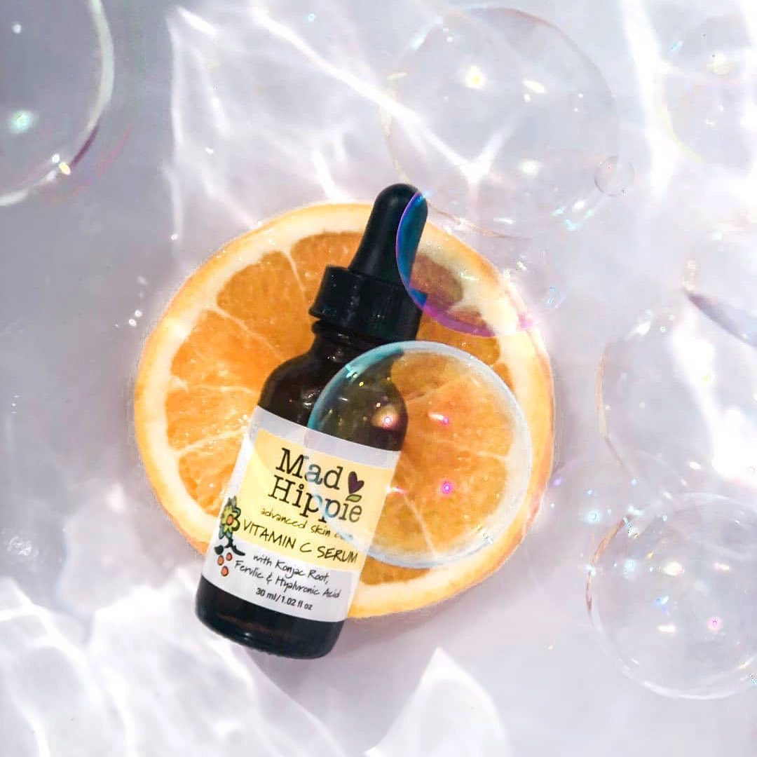 Chai serum Vitamin C Mad Hippie đặt trên lát cam, xung quanh có bọt bóng, biểu thị cho quy trình dưỡng da cơ bản giúp sáng mịn và mờ thâm, trả lời câu hỏi về cách dưỡng trắng an toàn và hiệu quả.