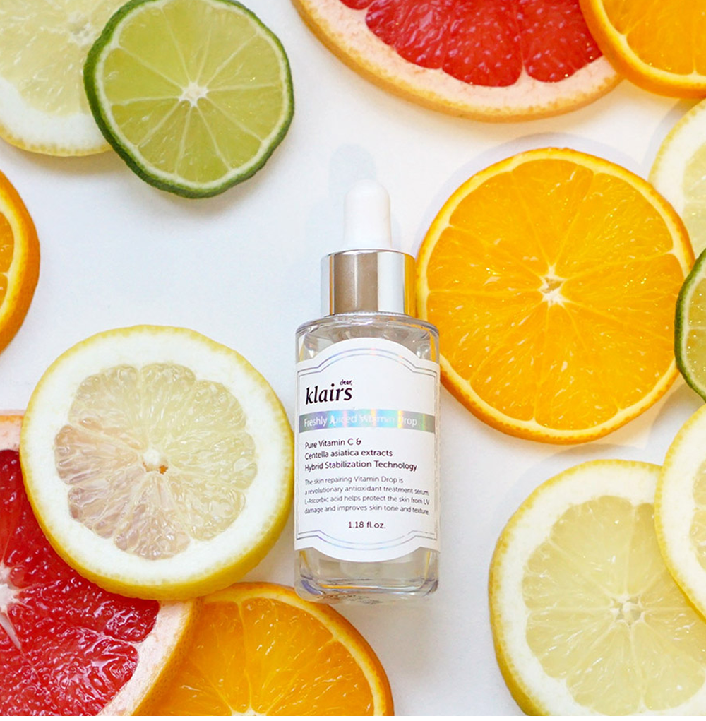 Serum dưỡng trắng Klairs Freshly Juiced Vitamin C nằm giữa những lát chanh, cam, bưởi, thể hiện sự tươi sáng và hiệu quả trong quy trình dưỡng da cơ bản. Halio Ion được khuyến nghị kết hợp với sản phẩm này để đạt hiệu quả tối đa.