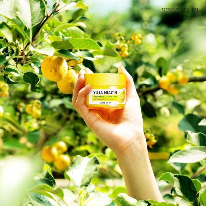 Nắm giữ kem dưỡng sáng da Yuja Niacin giữa khu vườn với nhiều quả chanh. Bài viết giới thiệu 6 sản phẩm skincare giúp dưỡng da trắng sáng trong mùa dịch.