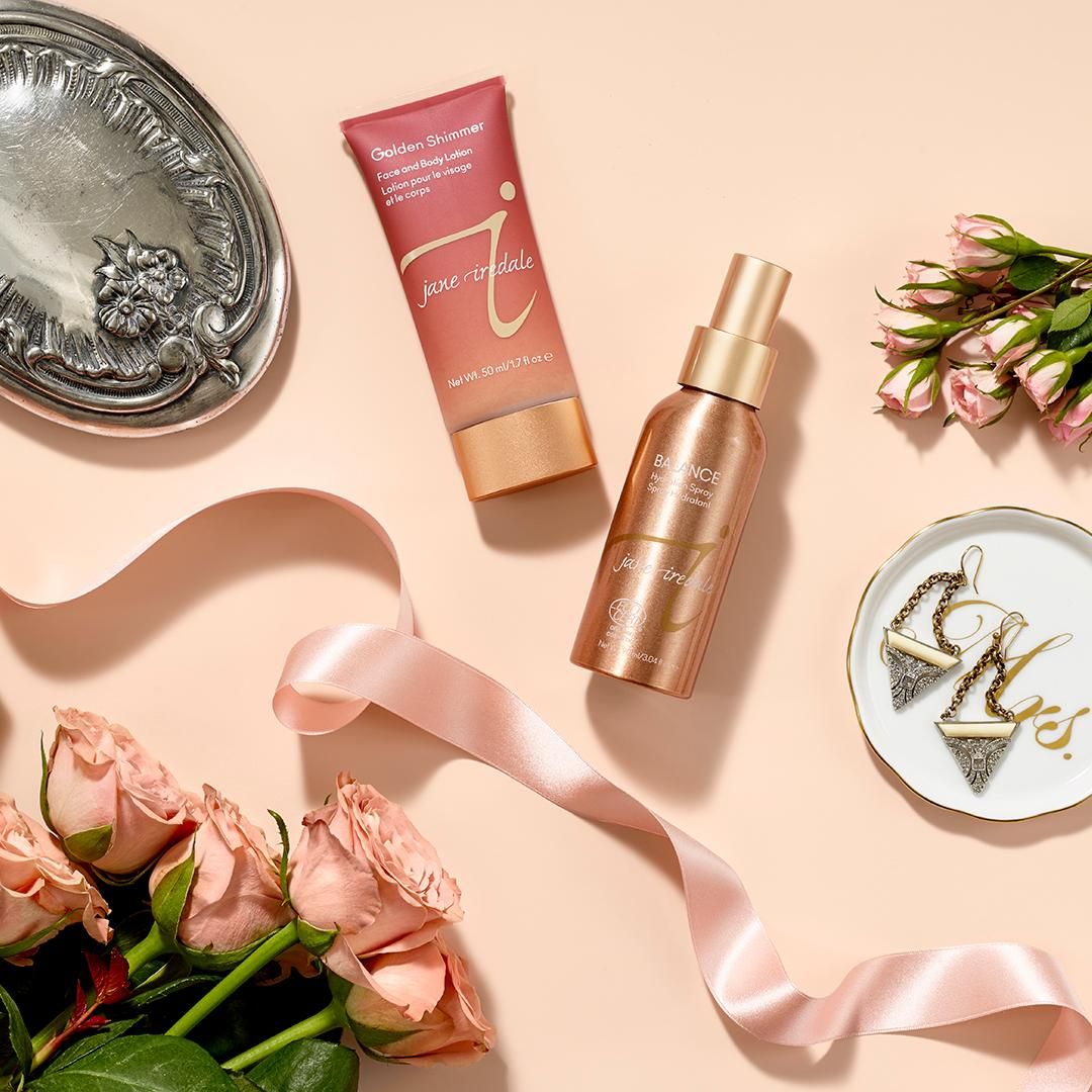 Top 6 dầu dưỡng ẩm toàn thân có nhũ cho cô nàng yêu thích vẻ đẹp rạng rỡ. Jane Iredale Golden Shimmer và Balance Body Spray được bài trí bắt mắt cùng hoa hồng và phụ kiện thời trang.