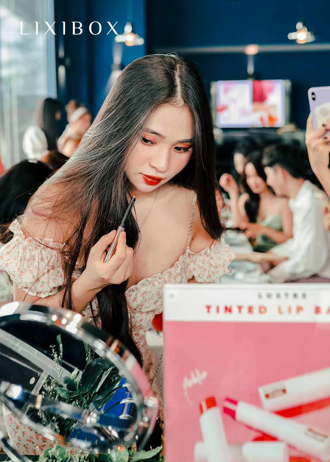 Trong bữa tiệc ra mắt sản phẩm mới của Lustre Makeup, một cô gái đang chăm chút trang điểm với son môi, tọa lạc trong không gian sang trọng, đầy sắc màu của Lustre Refillable Lipstick và Lustre Tinted Lip Balm. Sự kiện thu hút sự chú ý của nhiều influencers nổi bật.