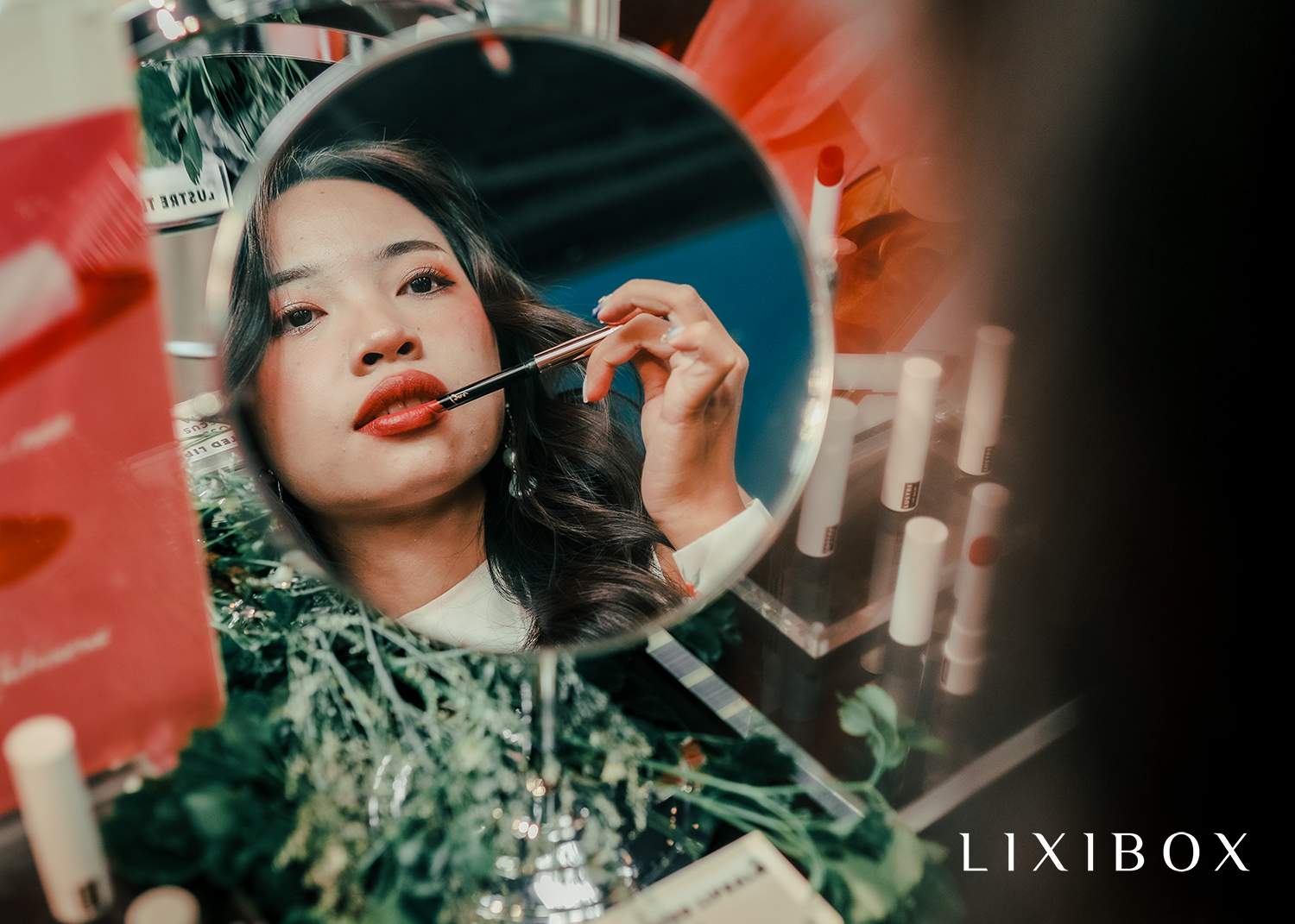 Bức ảnh ghi lại khoảnh khắc tại tiệc ra mắt sản phẩm baru của Lustre Makeup, nơi một cô gái đang trang điểm với son môi. Không gian tiệc đầy sắc màu với nhiều sản phẩm Lustre Lipstick và Lustre Tinted Lip Balm, thu hút sự chú ý của các nàng yêu thích trang điểm.