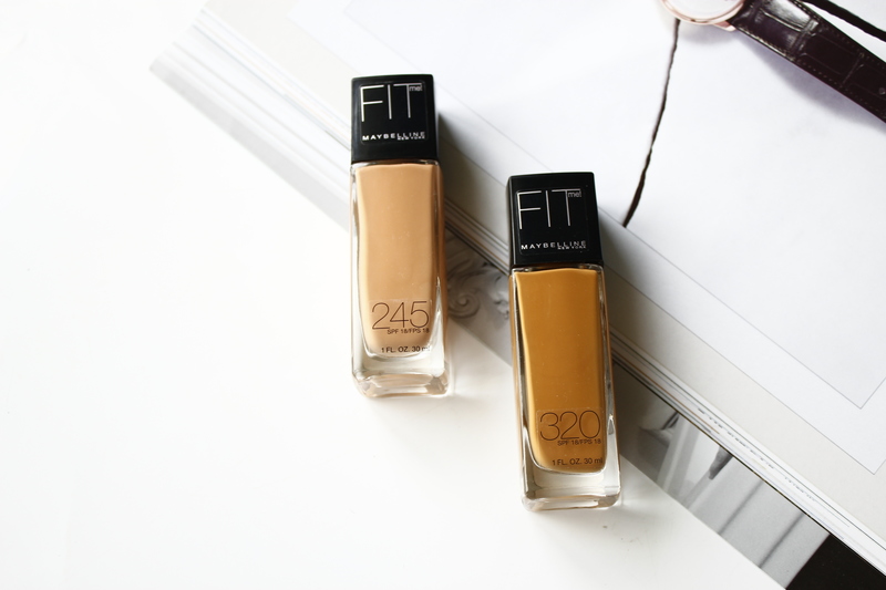 Hai lọ kem nền Maybelline Fit Me với mã 245 và 320, đặt trên một tạp chí làm đẹp. Bài viết giới thiệu 10 sản phẩm drugstore không thể bỏ qua. Tìm hiểu thêm về GWP, GWP Vietnam và GWP Lixibox.