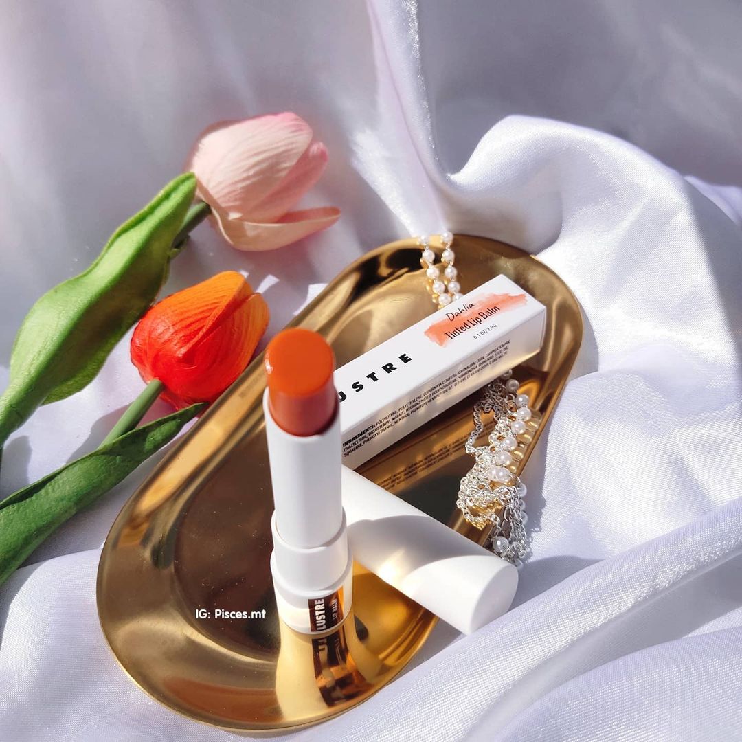 Son dưỡng có màu Lustre Tinted Lip Balm với chất lượng vượt trội và thiết kế tinh tế, cùng với hoa và trang sức xung quanh, thể hiện sự yêu thích và đánh giá cao từ người dùng trong bài review mỹ phẩm.