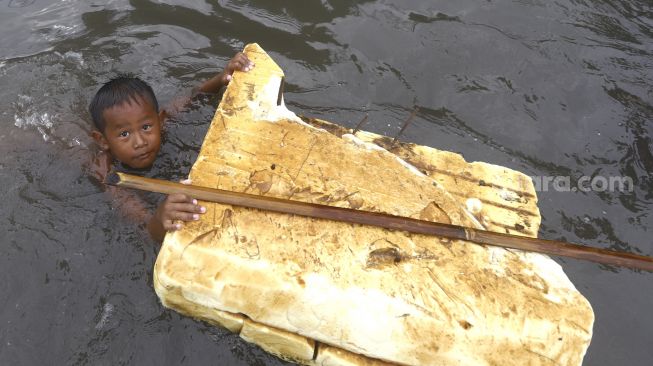 Bocah berenang saat banjir rob di kawasan Pelabuhan Nizam Zachman, Muara Baru, Jakarta Utara, Jumat (5/6). . [Suara.com/Angga Budhiyanto]