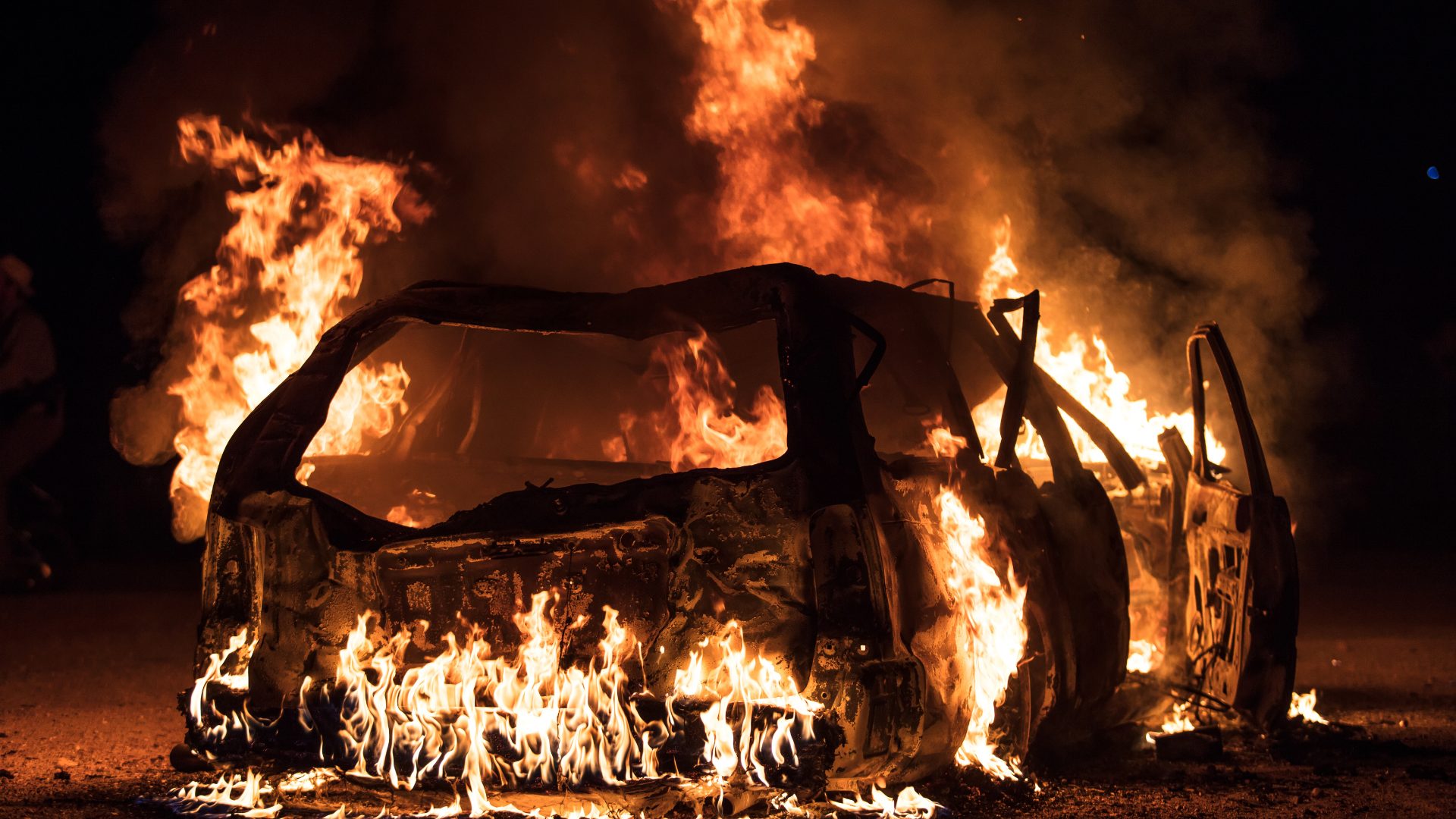A dramatic scene of an electric vehicle engulfed in flames, showcasing the intense fire and smoke rising from the burning car. The image highlights the potential risks associated with electric vehicle fires, drawing attention to safety concerns.